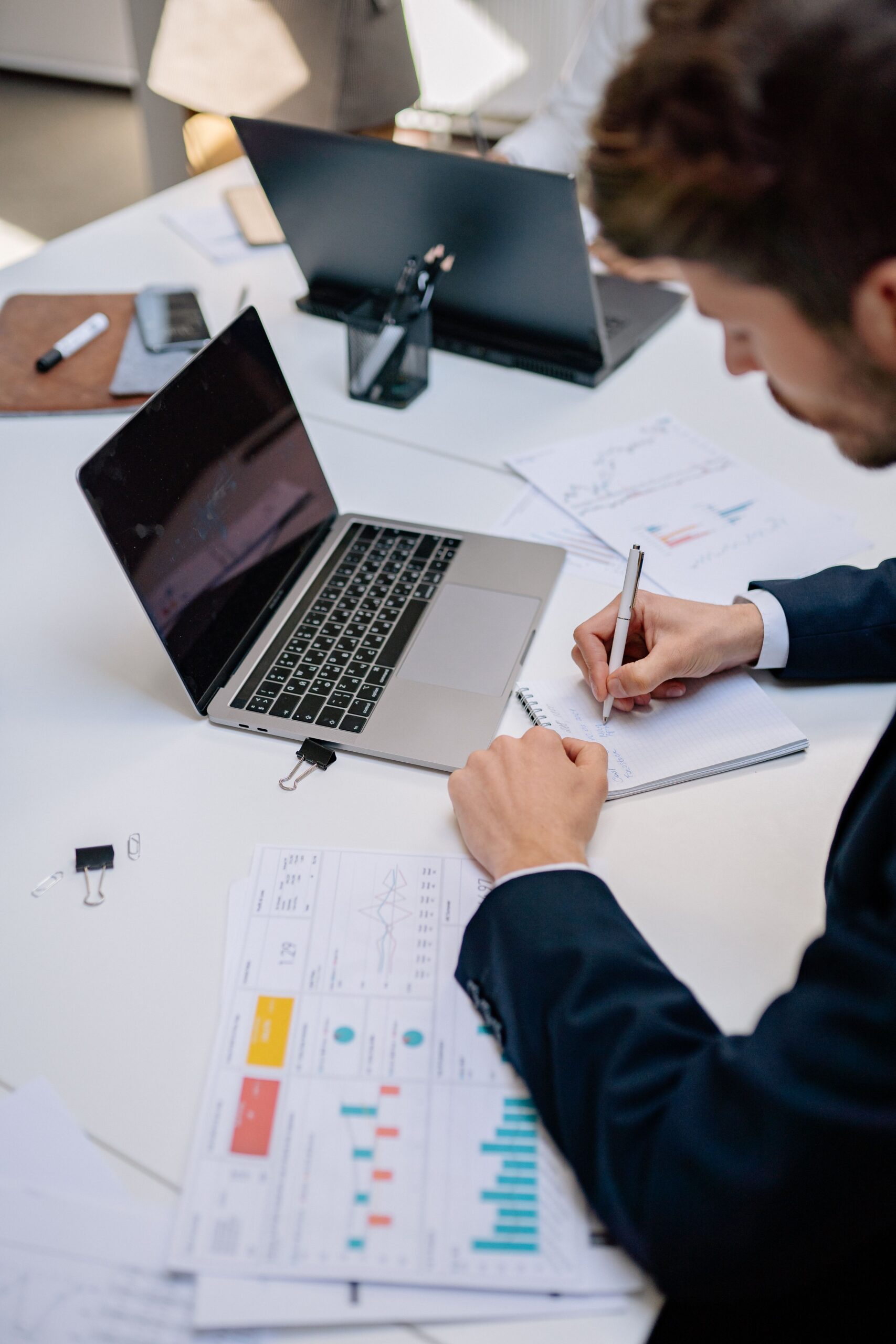 Business professional taking notes with a laptop and documents on a desk. Modern workspace concept.